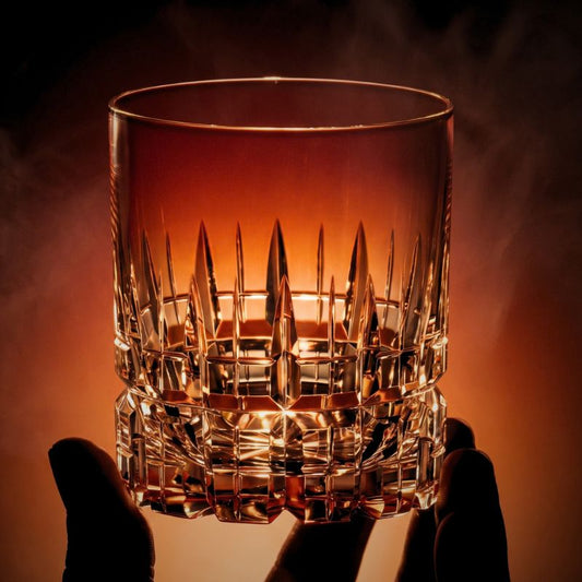 Crystal whiskey glass held up to warm light, its pointed spire cuts glowing amber