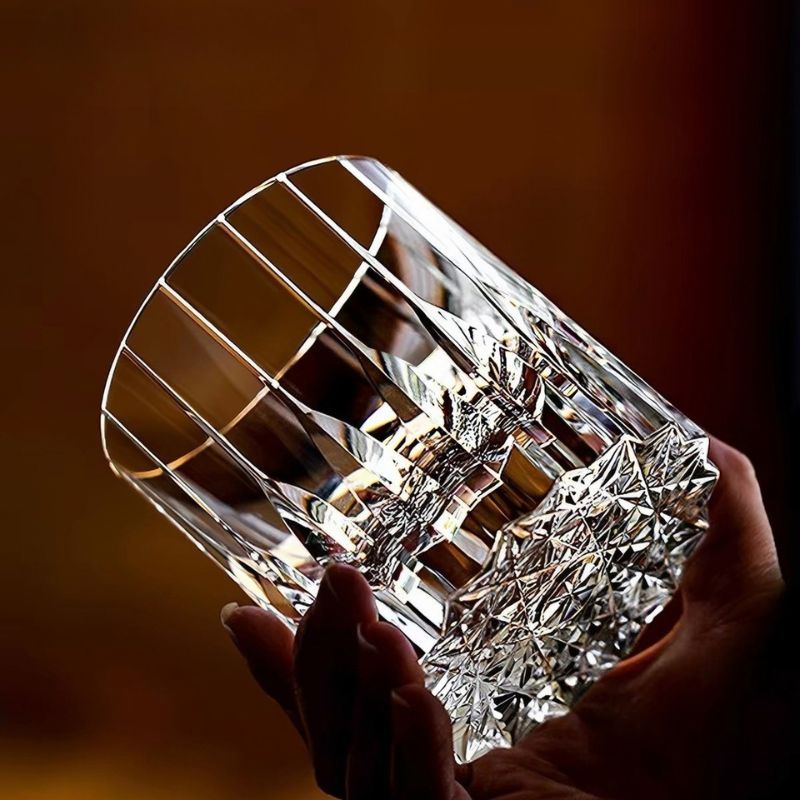 Hand holding a heavy hand-cut crystal whiskey glass against warm light
