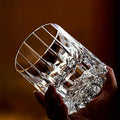 Hand holding a heavy hand-cut crystal whiskey glass against warm light