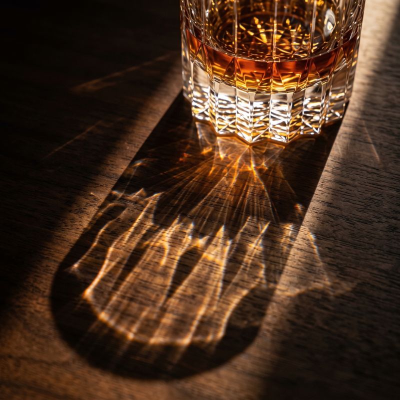 Light shining through a crystal whiskey glass onto a wooden table