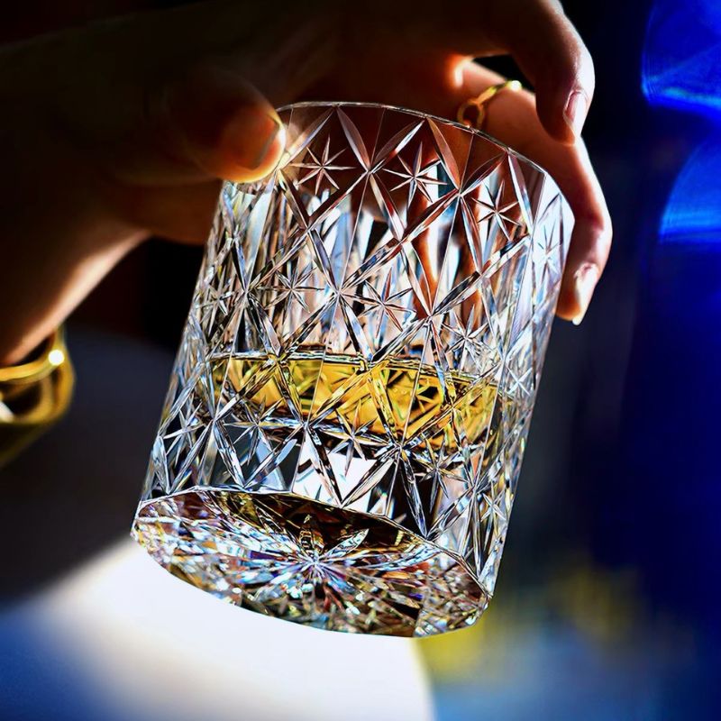 Hand tilting the Polaris hand-cut crystal whiskey glass with whiskey, showing the starburst cut on the base