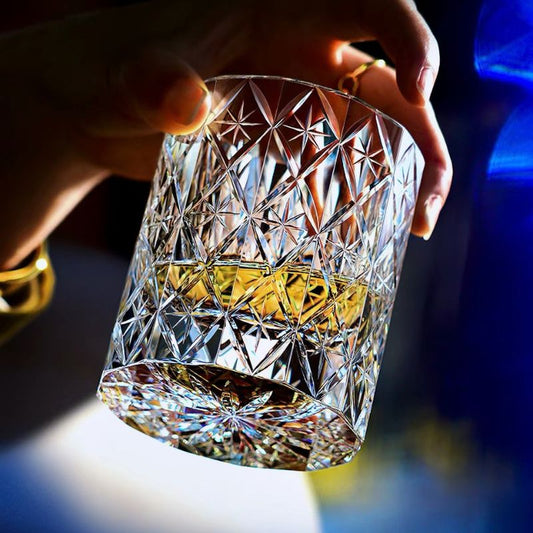 Hand tilting the Polaris hand-cut crystal whiskey glass with whiskey, showing the starburst cut on the base